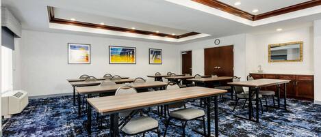 Un salón de conferencias con varias mesas y sillas, un reloj y cuadros en la pared.