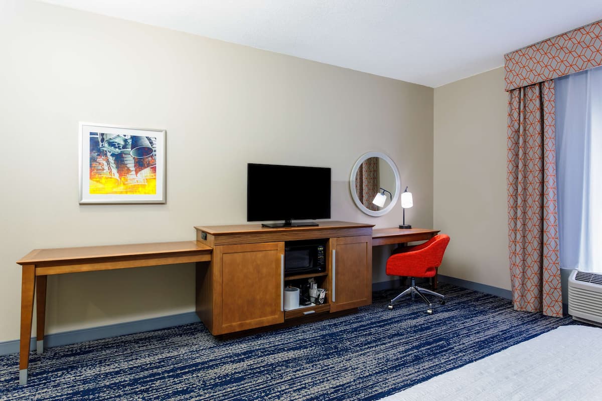 Habitación de hotel con un escritorio de madera, televisor, espejo, una silla roja y una cortina estampada.