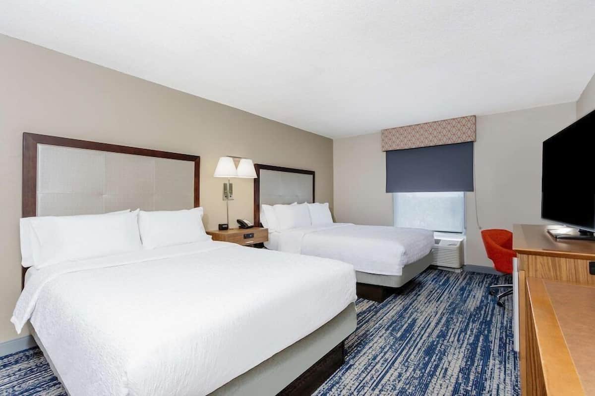 Una habitación de hotel con dos camas, un escritorio, una silla, un televisor y una lámpara.
