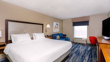 A hotel room with a large bed, a desk with a television, a blue sofa, and a window with a view.