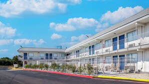 A motel with multiple rooms, a covered parking area, and a clear blue sky with clouds. - Motel 6 Fort Worth, TX - East (Fort Worth)