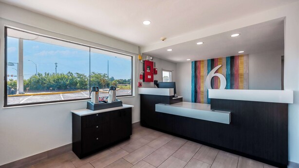 A reception area with a large window, a reception desk, a black cabinet, and a colorful wall decoration. - Motel 6 Fort Worth, TX - East (Fort Worth)