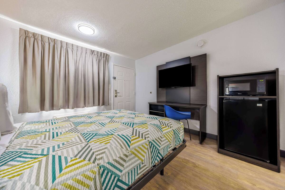 A hotel room with a bed, a desk, a TV, and a refrigerator.