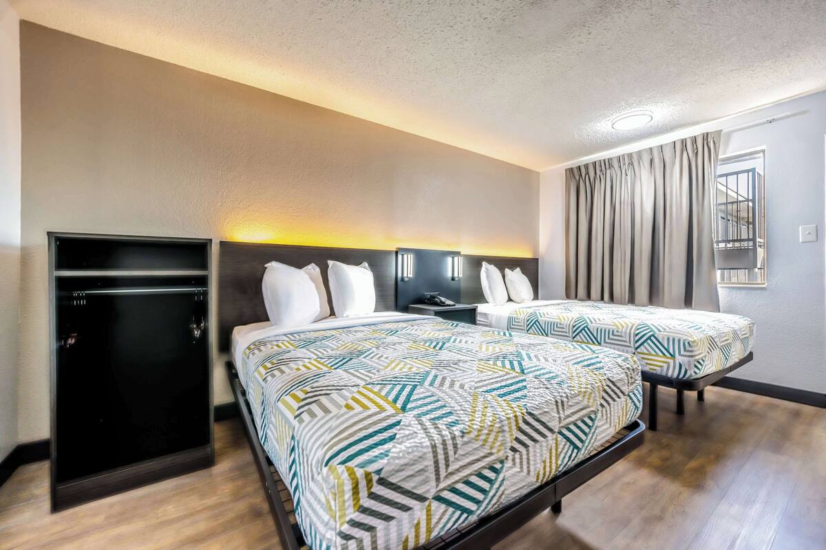 A hotel room with two beds, a TV, a desk, and a window with curtains.