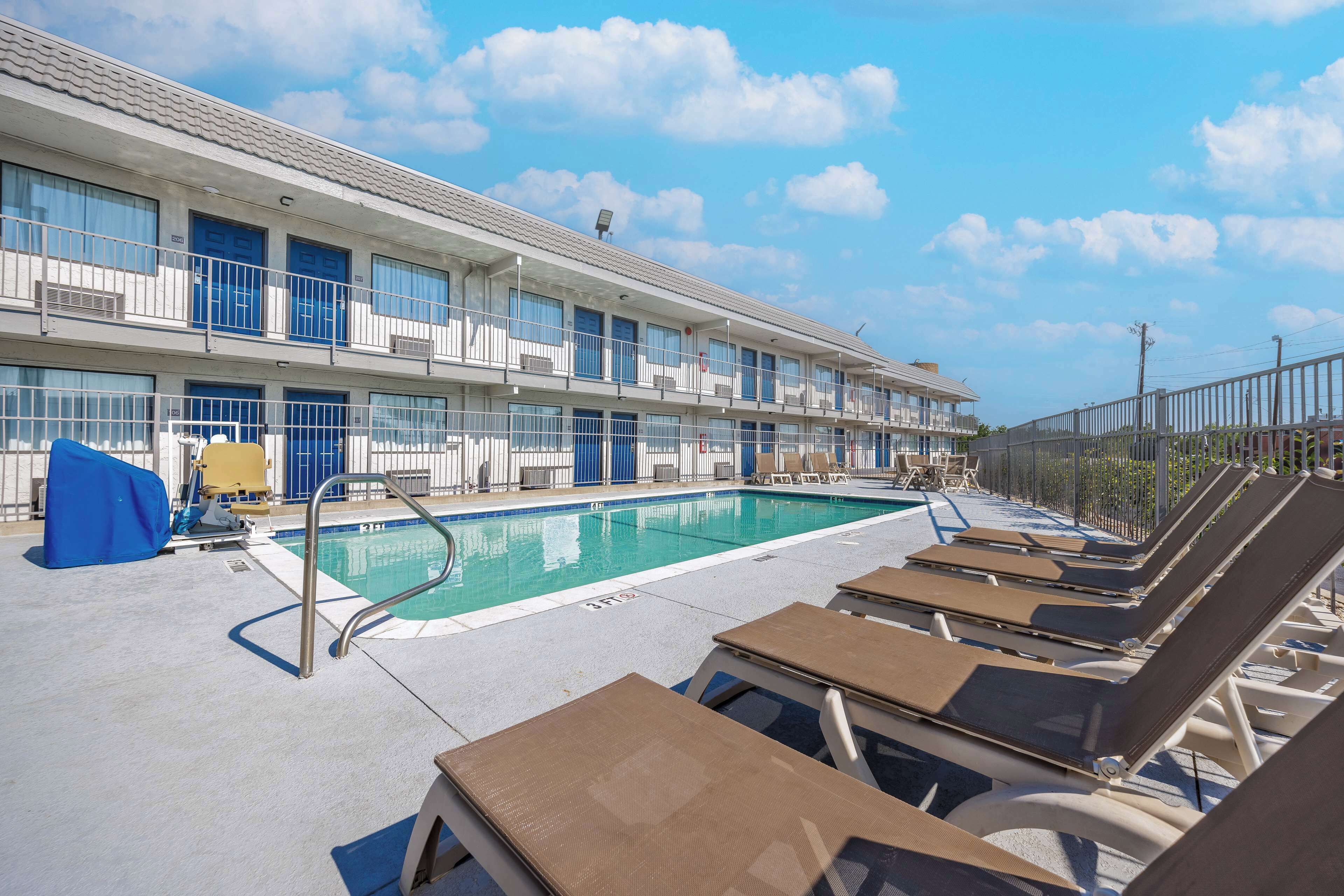 A hotel with a swimming pool, lounge chairs, and a covered seating area.