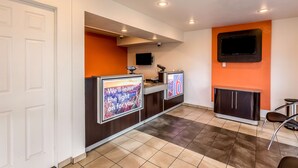 A reception area with a counter, a TV mounted on the wall, and a seating area with a chair. - Motel 6 El Paso, TX - East (El Paso)