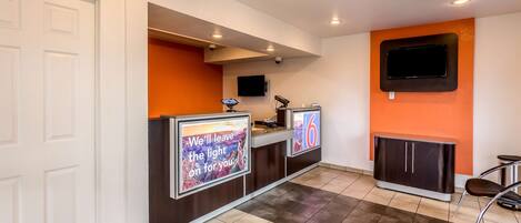 A reception area with a counter, a TV mounted on the wall, and a seating area with a chair.
