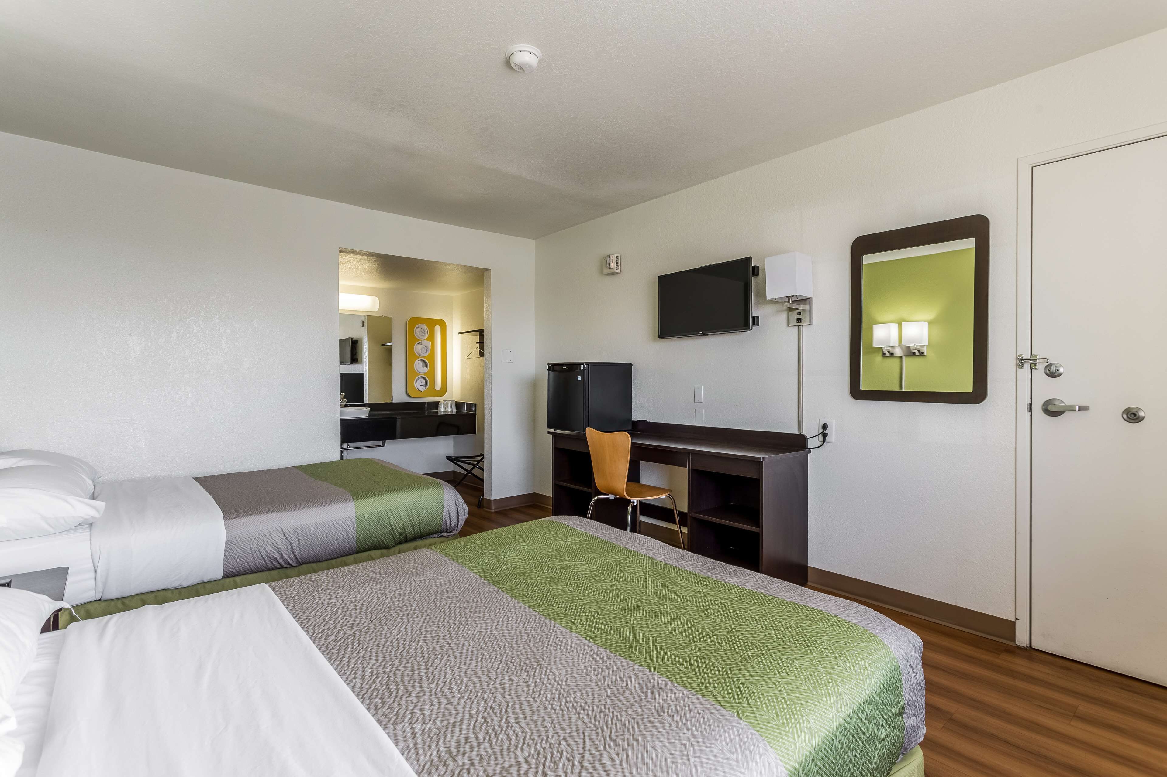A hotel room with two beds, a desk, a television, a mirror, and a wardrobe.