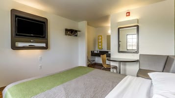 Habitación de hotel con cama, escritorio, silla, televisor y espejo.