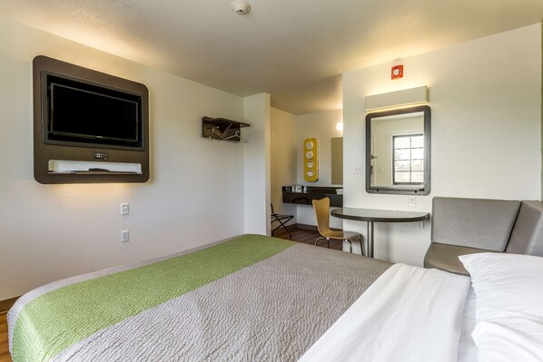 A hotel room with a bed, a desk, a chair, a TV, and a mirror.
