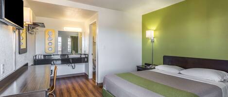 A hotel room with a bed, a desk, a chair, a mirror, and a green wall.