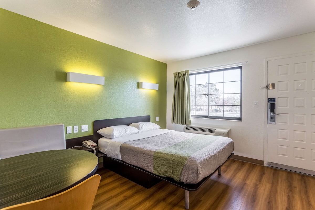 A hotel room with a bed, bedside table, chair, and a window with curtains.