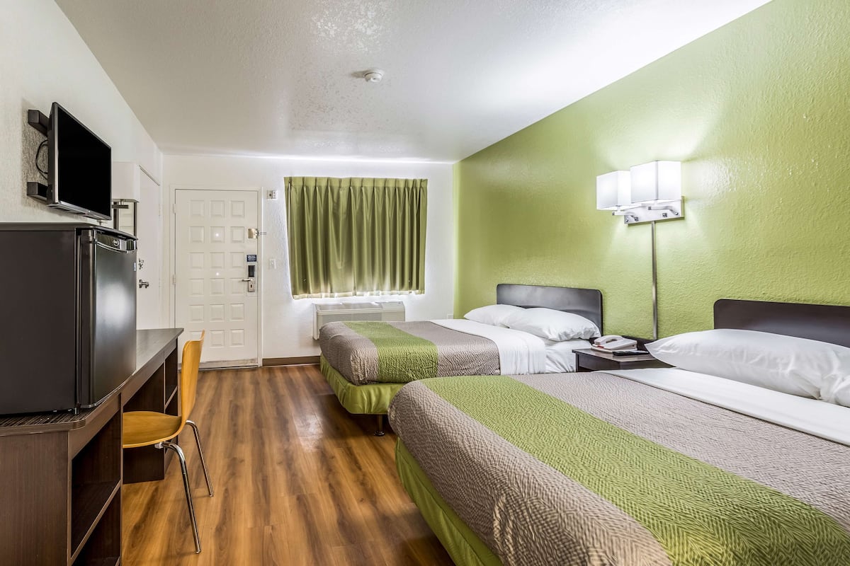 A hotel room with two beds, a desk with a television, a chair, and a window with curtains.