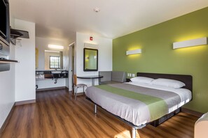 A hotel room with a bed, a desk, a chair, and a bathroom.