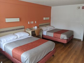 A hotel room with two beds, a desk, a chair, and a telephone.