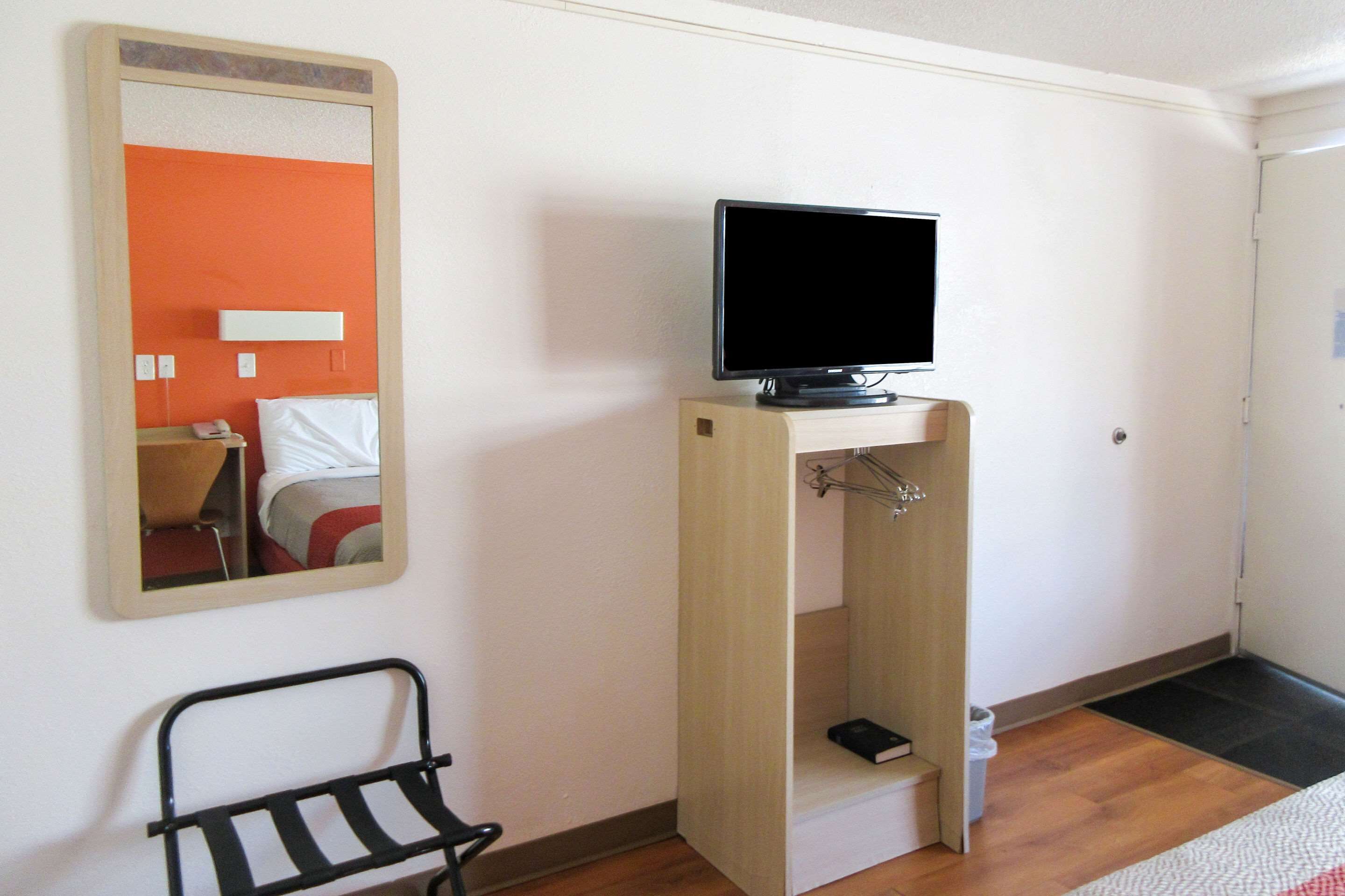 A room with a bed, a television on a stand, a mirror, and a small black chair.
