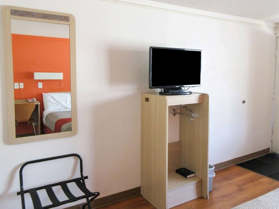 A room with a bed, a television on a stand, a mirror, and a small black chair.