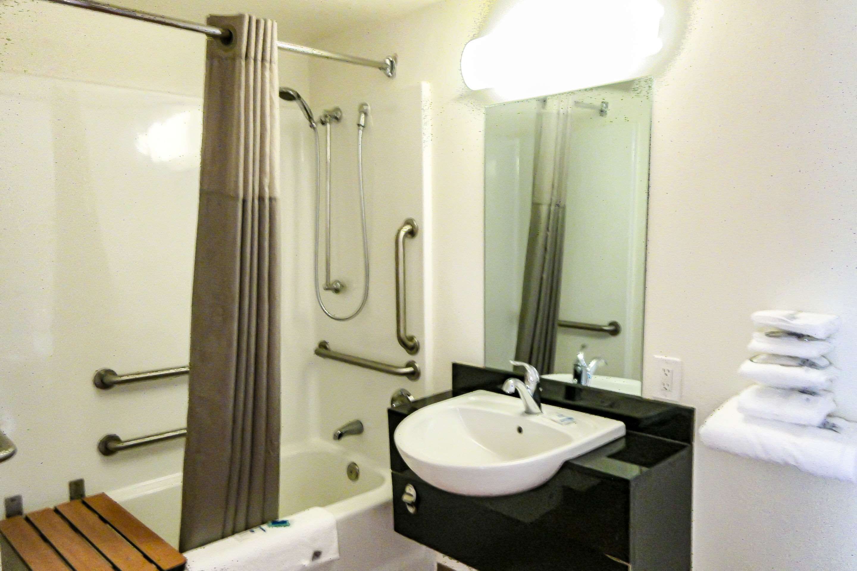 Une salle de bain équipée d’une douche, de barres d’appui, d’un lavabo et d’un miroir.