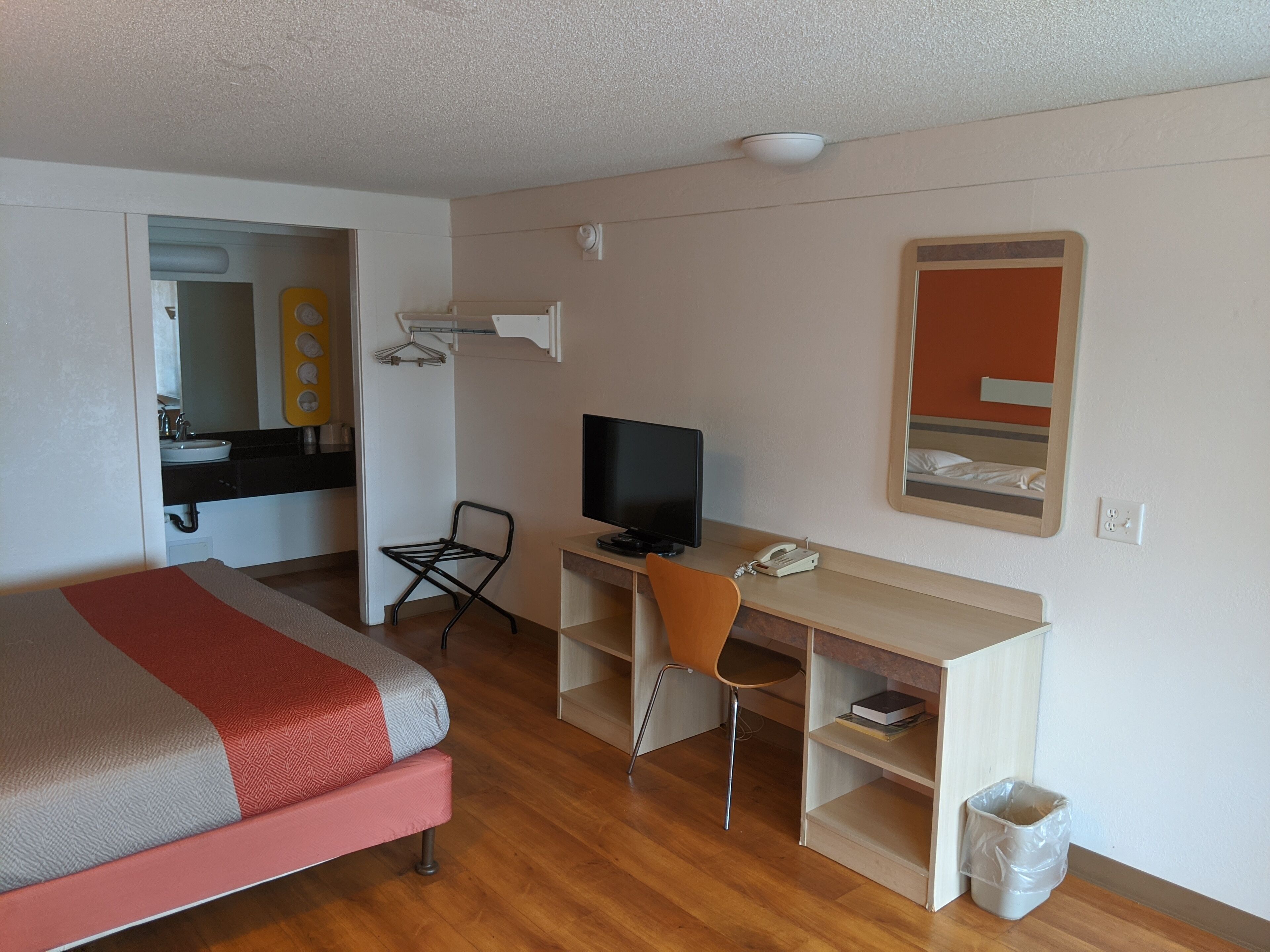 Une chambre d’hôtel équipée d’un lit, d’un bureau avec un ordinateur, d’une chaise, d’une télévision et d’un miroir.