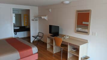 A hotel room with a bed, a desk with a computer, a chair, a TV, and a mirror.