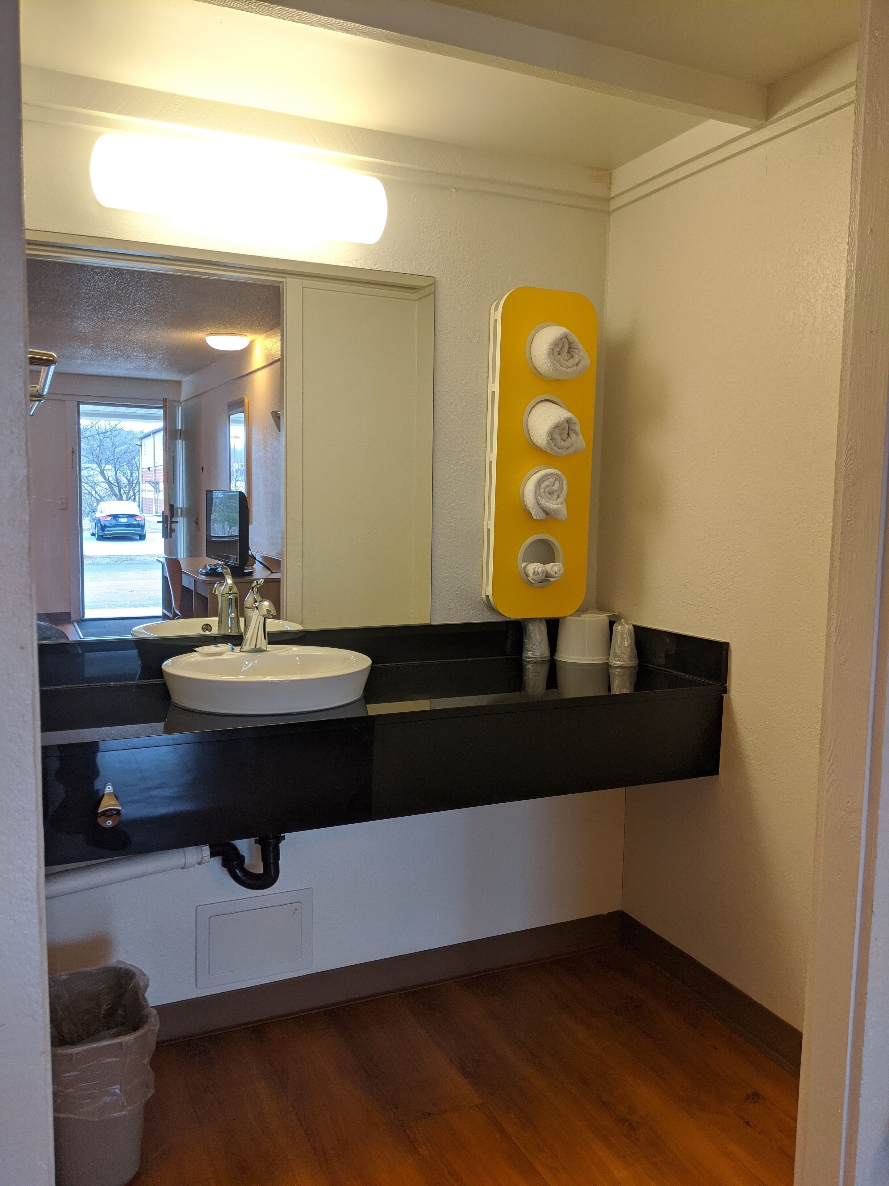 A bathroom with a black countertop, white sink, and a mirror above it. There is a yellow towel rack with three towels and a small window above the sink.