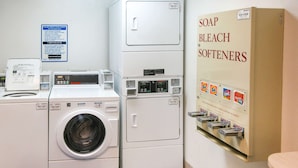 A laundry area with a front-loading washer and dryer, a soap and bleach dispenser, and a sign with emergency contact information.