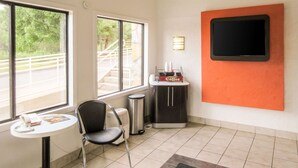 A small room with a window, a chair, a table, a coffee station, and a TV mounted on the wall.