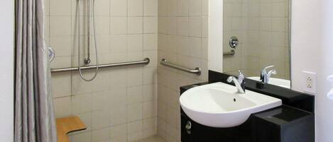 A bathroom with a white sink, black countertop, and a mirror. There are grab bars on the walls and a showerhead.