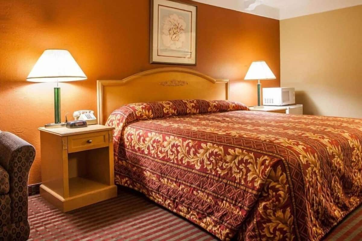 A hotel room with a large bed, two bedside tables, a chair, and a framed picture on the wall.