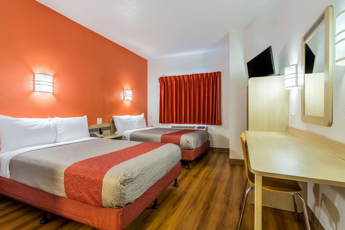 A hotel room with two beds, a desk, and a mirror.