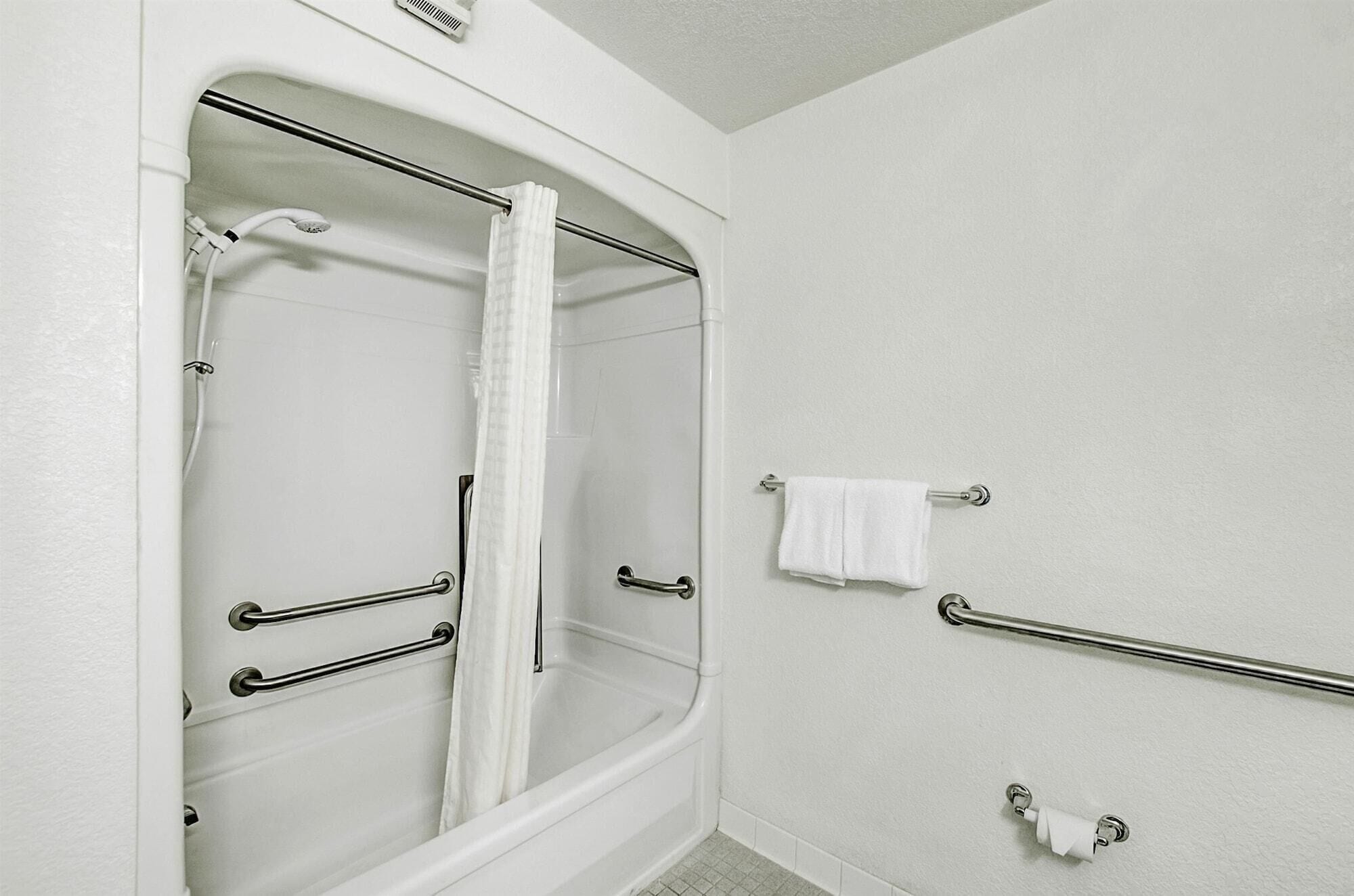 A bathroom with a walk-in shower, grab bars, and a towel rack.