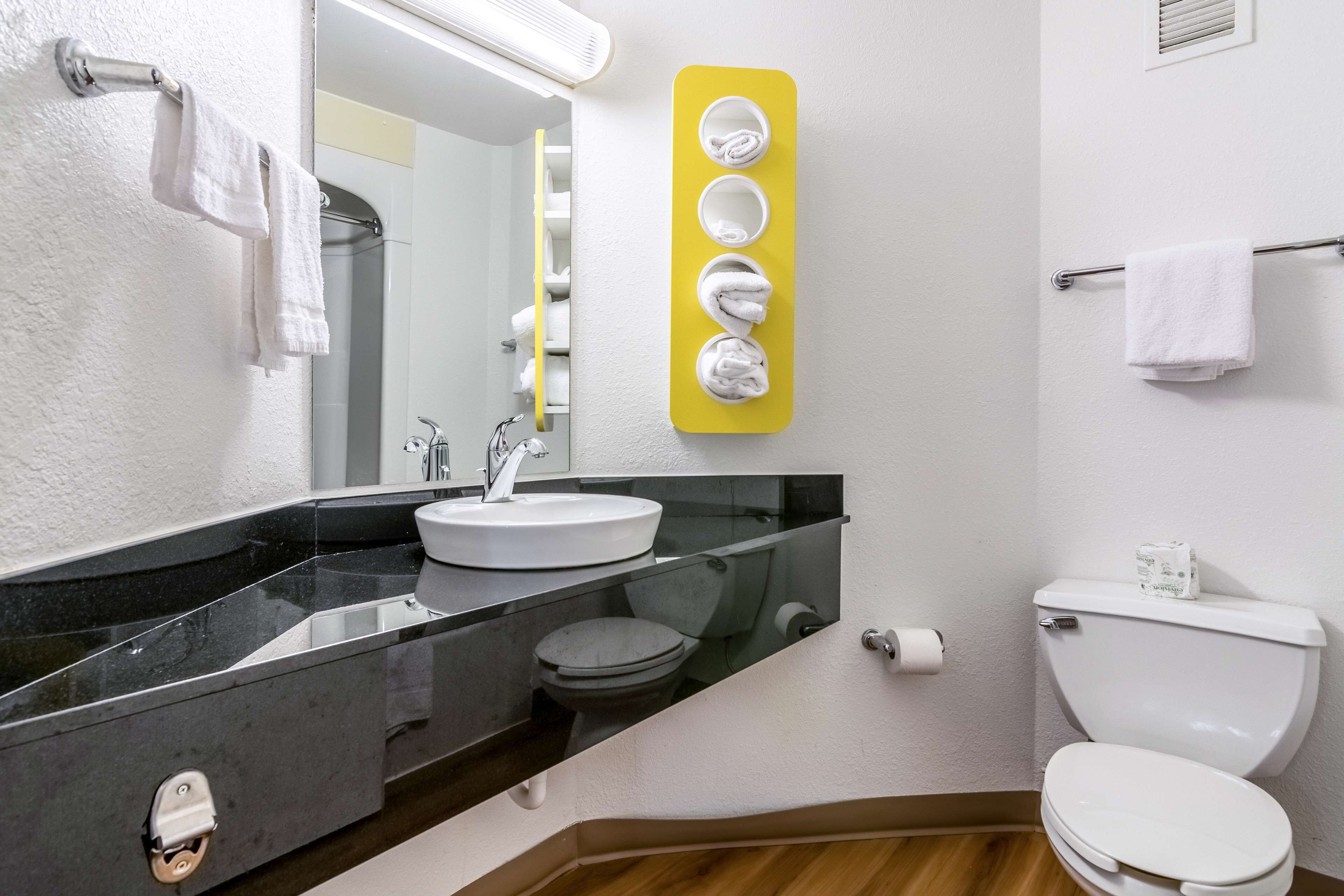 Ein modernes Badezimmer mit schwarzem Waschtisch, weißem Waschbecken und Toilette. Ein Spiegel mit Handtuchhalter und ein gelber Handtuchwärmer sind vorhanden.