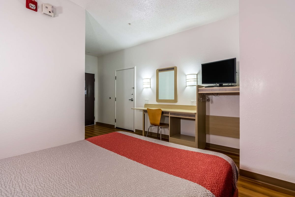 A hotel room with a bed, a desk, a chair, a television, and a mirror.
