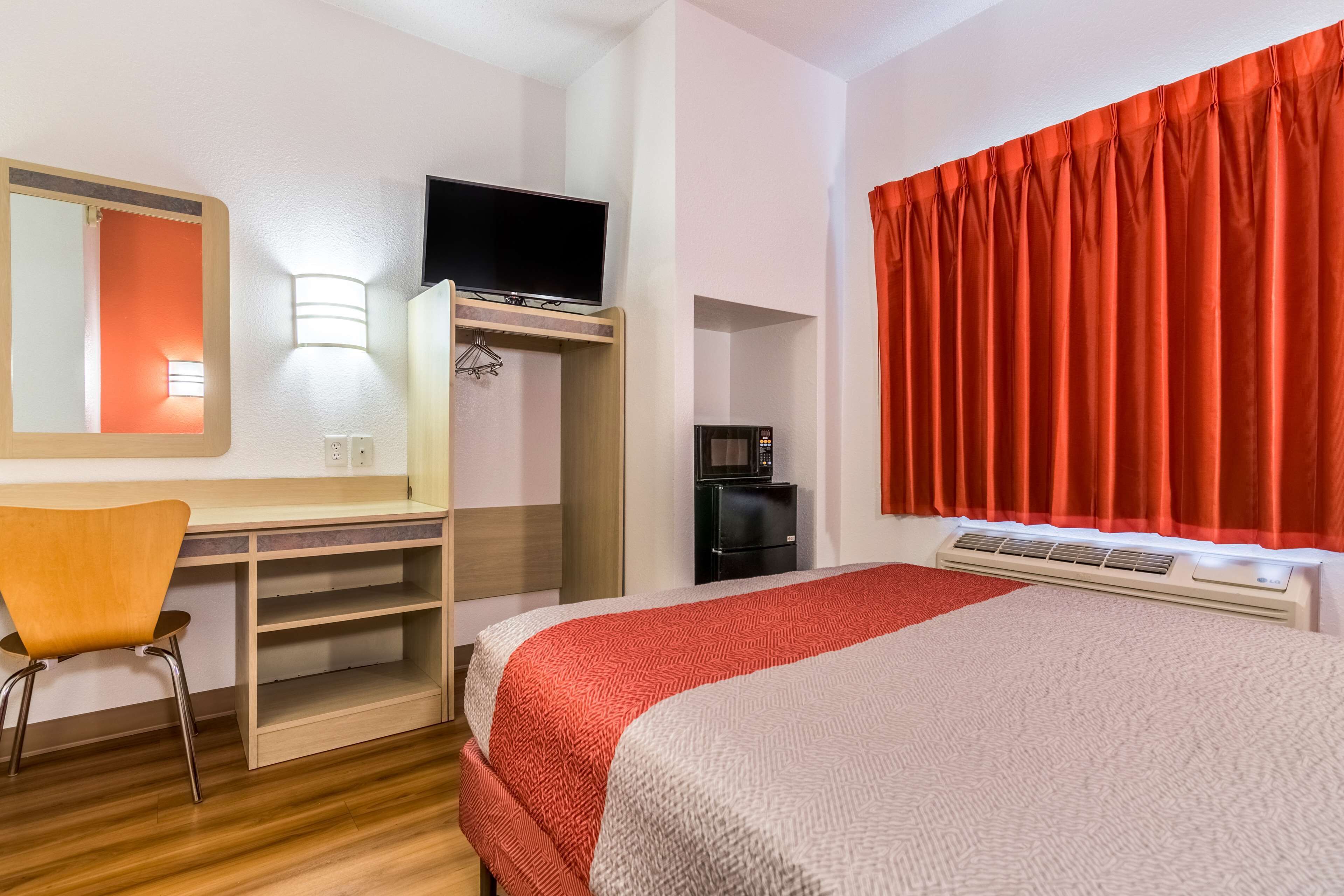 Hotelkamer met een bed, een bureau met stoel, een televisie, een koffiezetapparaat en een rood gordijn.