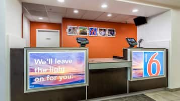 A hotel reception area with a modern design, featuring a reception desk, a digital display, and a wall-mounted security camera.