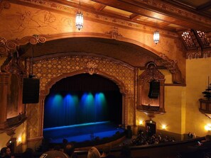 Un interior de teatro ornamentado con un escenario, asientos para el público e iluminación decorativa.