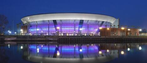 A modern, circular building with a glass facade and a reflection in the water in front.