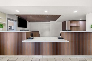 Un área de recepción con diseño moderno, que presenta un mostrador de madera, un televisor de pantalla plana montado en la pared e iluminación empotrada en el techo.