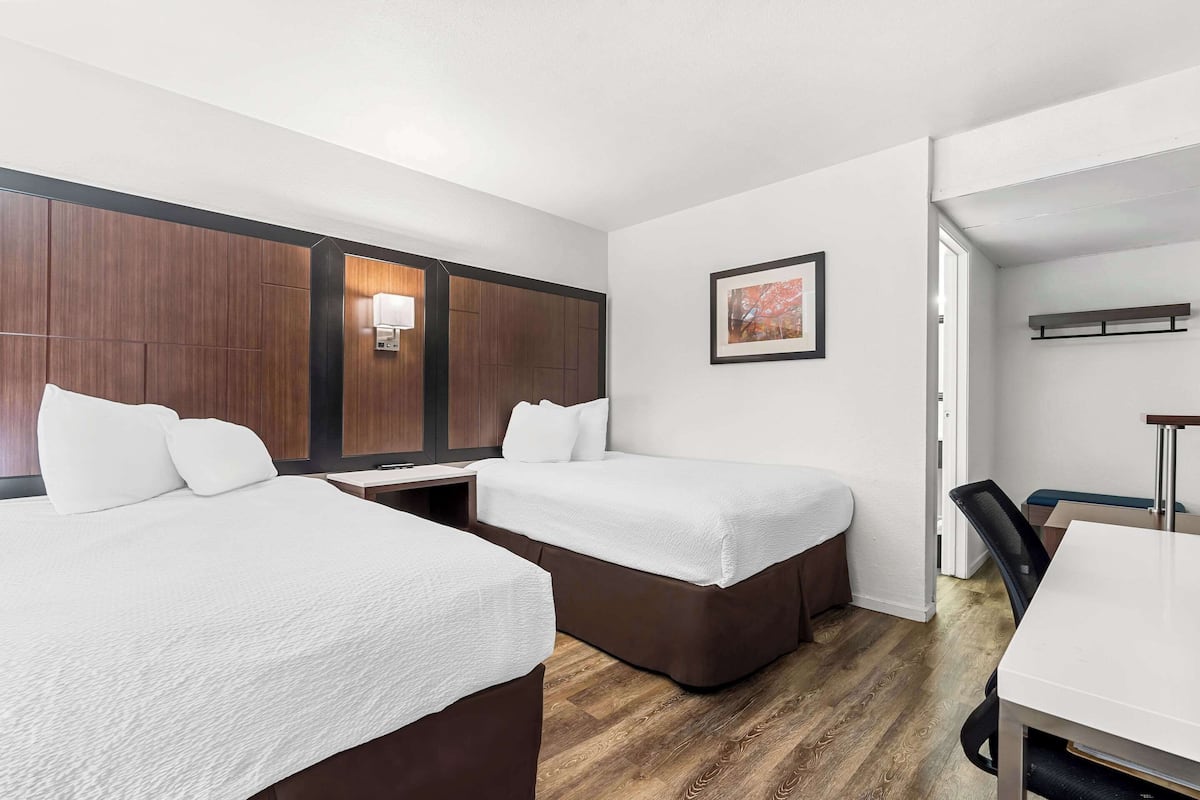 A hotel room with two beds, a desk, and a chair.