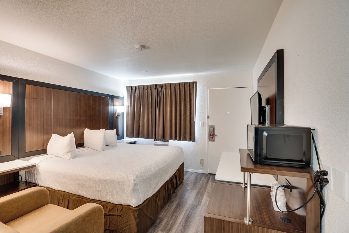 Una habitación de hotel con una cama grande, un escritorio, una silla, un televisor y un espejo.