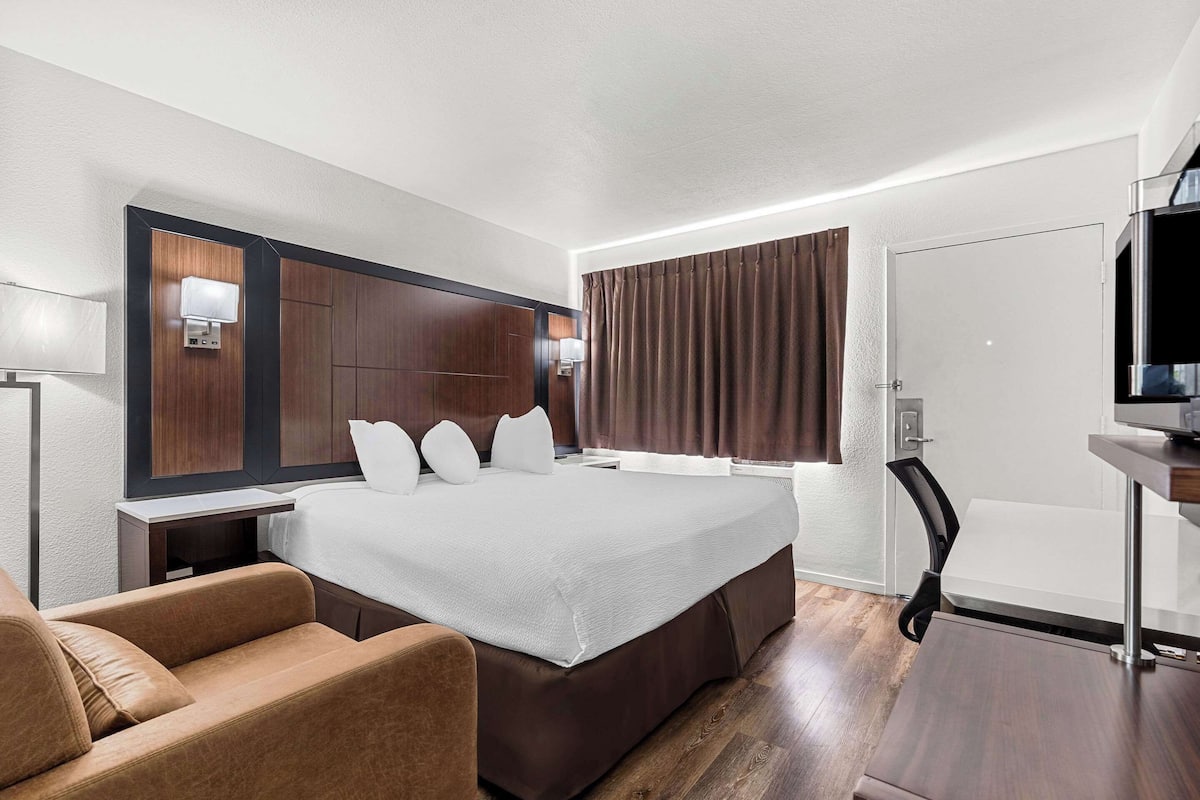 A modern hotel room with a large bed, a desk, a chair, and a television.