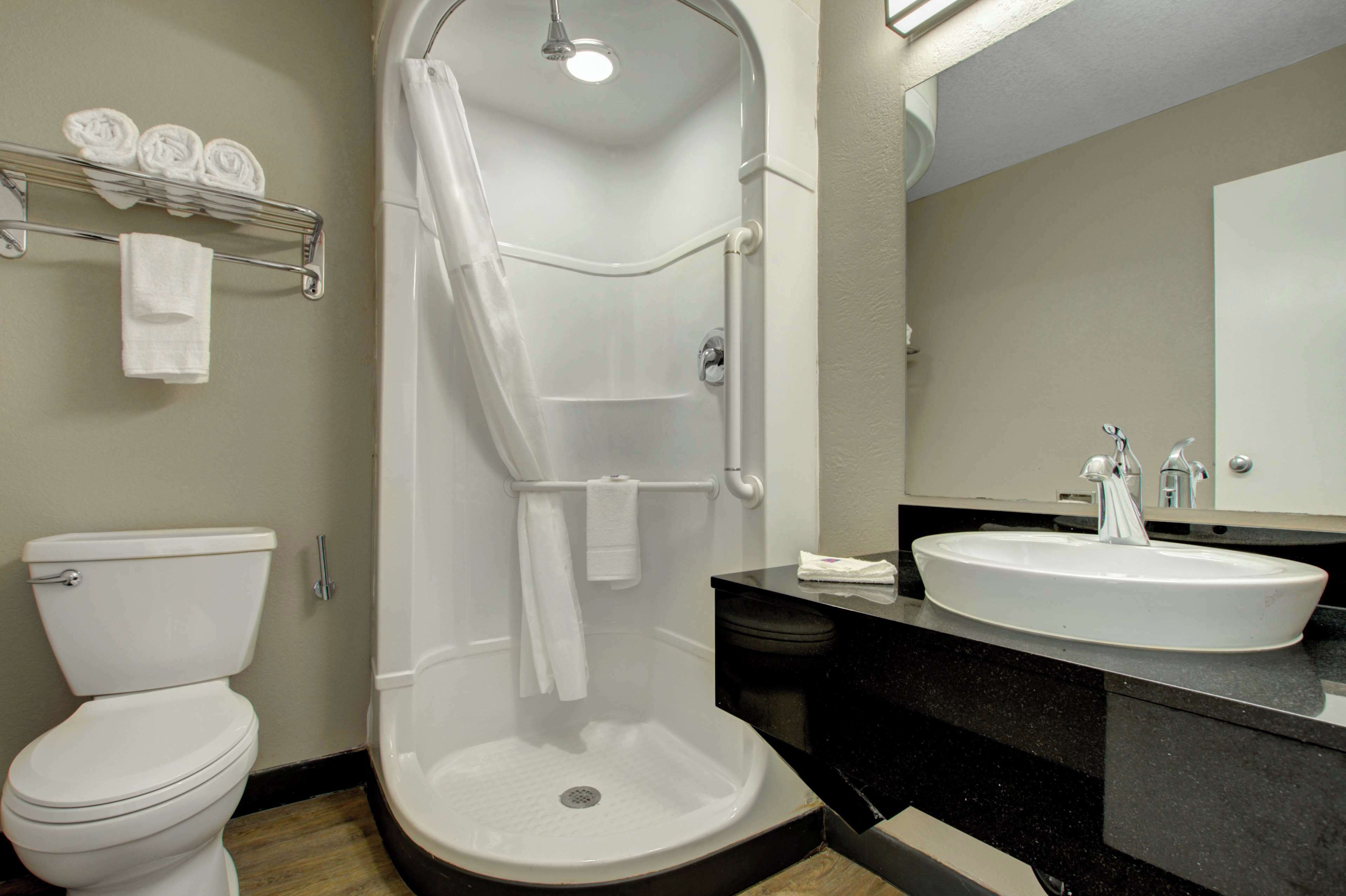 Une salle de bain comprenant des toilettes, une douche à l’italienne, un lavabo et un porte-serviettes avec des serviettes.