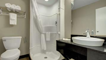 Une salle de bain comprenant des toilettes, une douche à l’italienne, un lavabo et un porte-serviettes avec des serviettes.