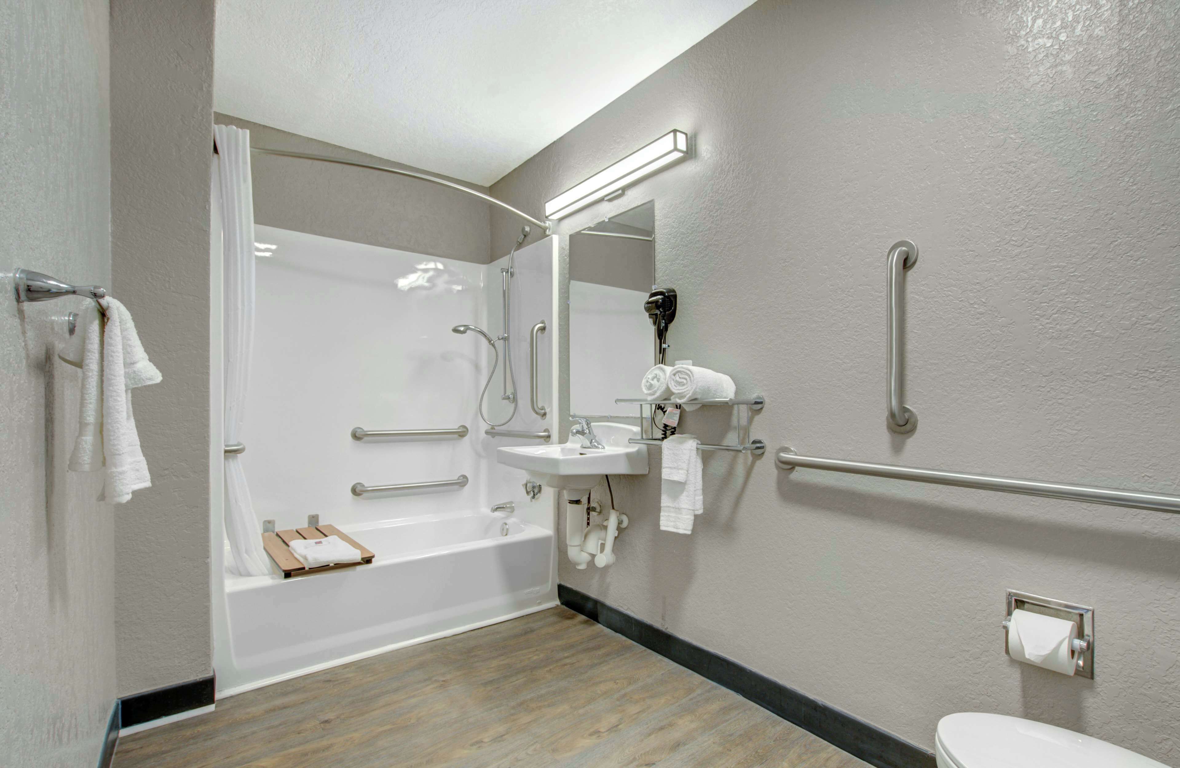 Un baño moderno con cabina de ducha, barras de apoyo, lavamanos e inodoro.