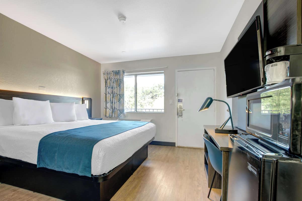A hotel room with a bed, a desk with a computer, a flat-screen TV, and a window with curtains.