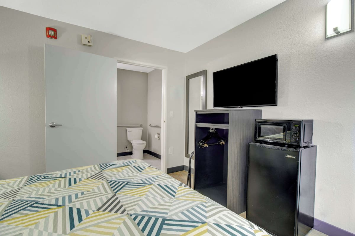 A hotel room with a bed, a refrigerator, a microwave, a television, and a bathroom visible through an open door.