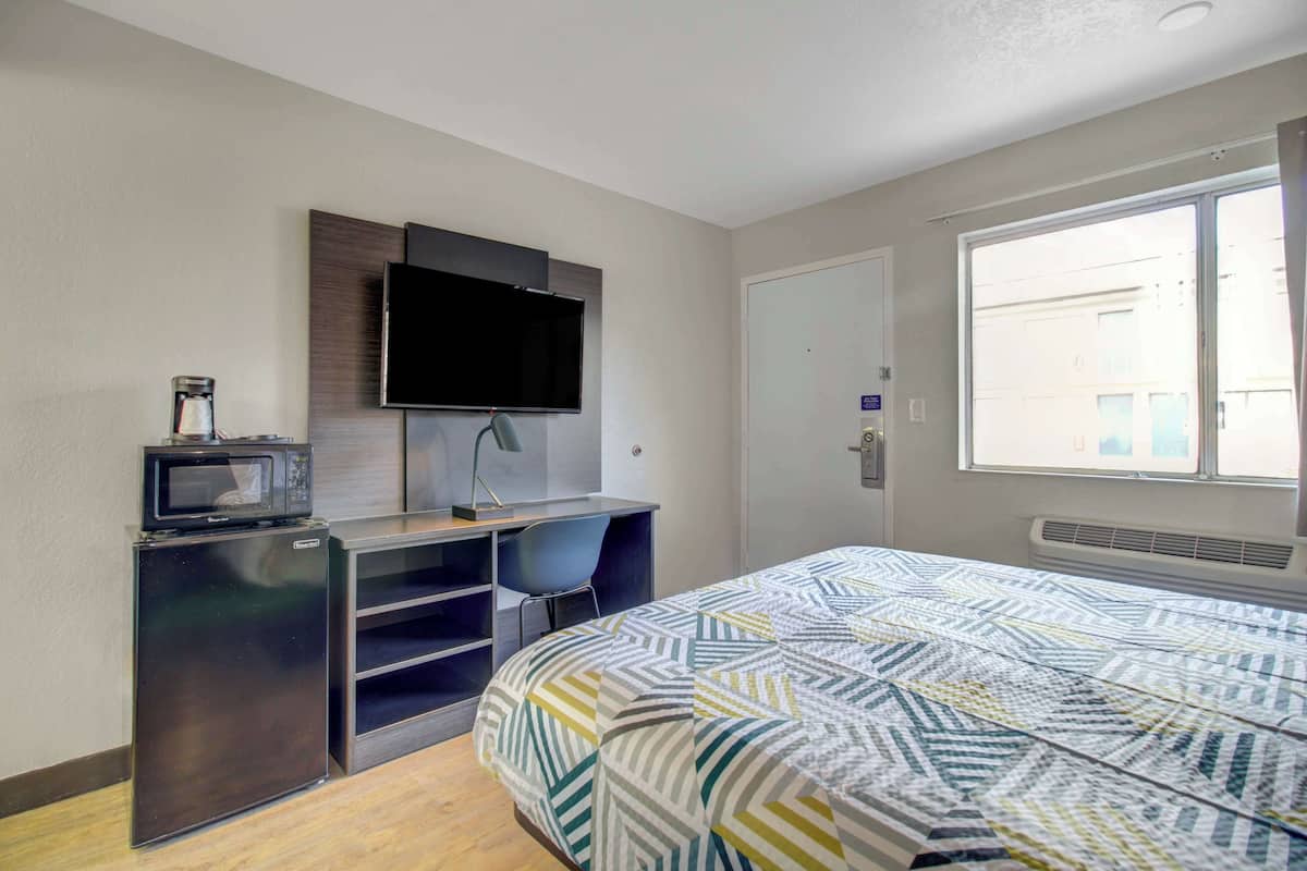 A compact hotel room with a bed, a desk with a chair, a television, and a microwave.