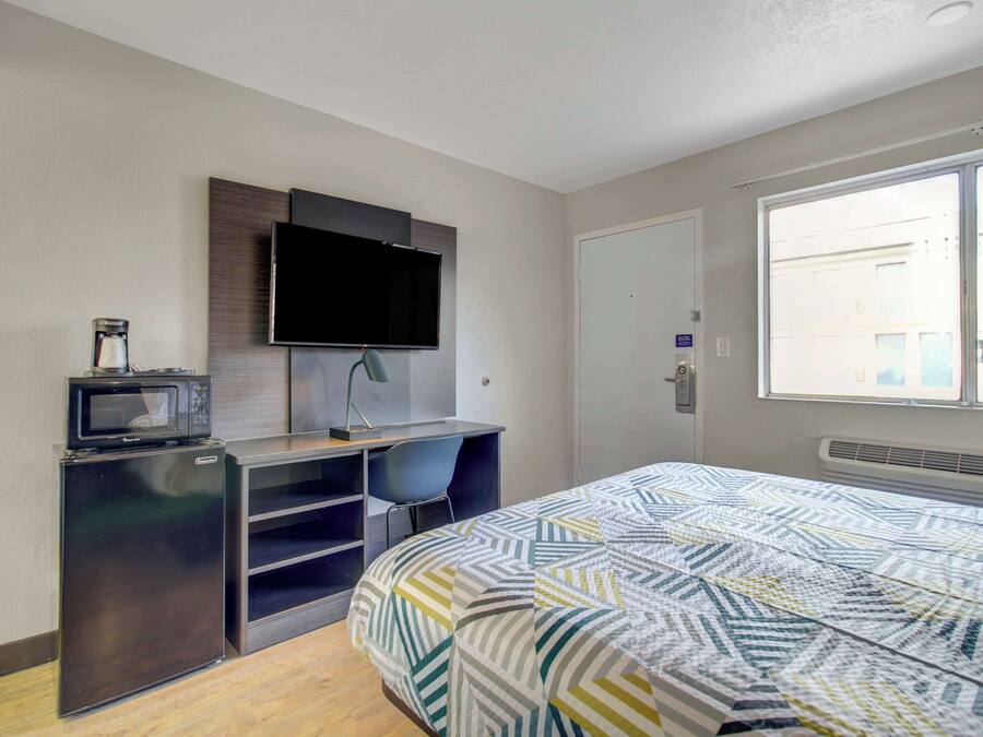 Ein kleines Hotelzimmer mit Bett, Schreibtisch mit Stuhl, Fernseher und Mikrowelle.
