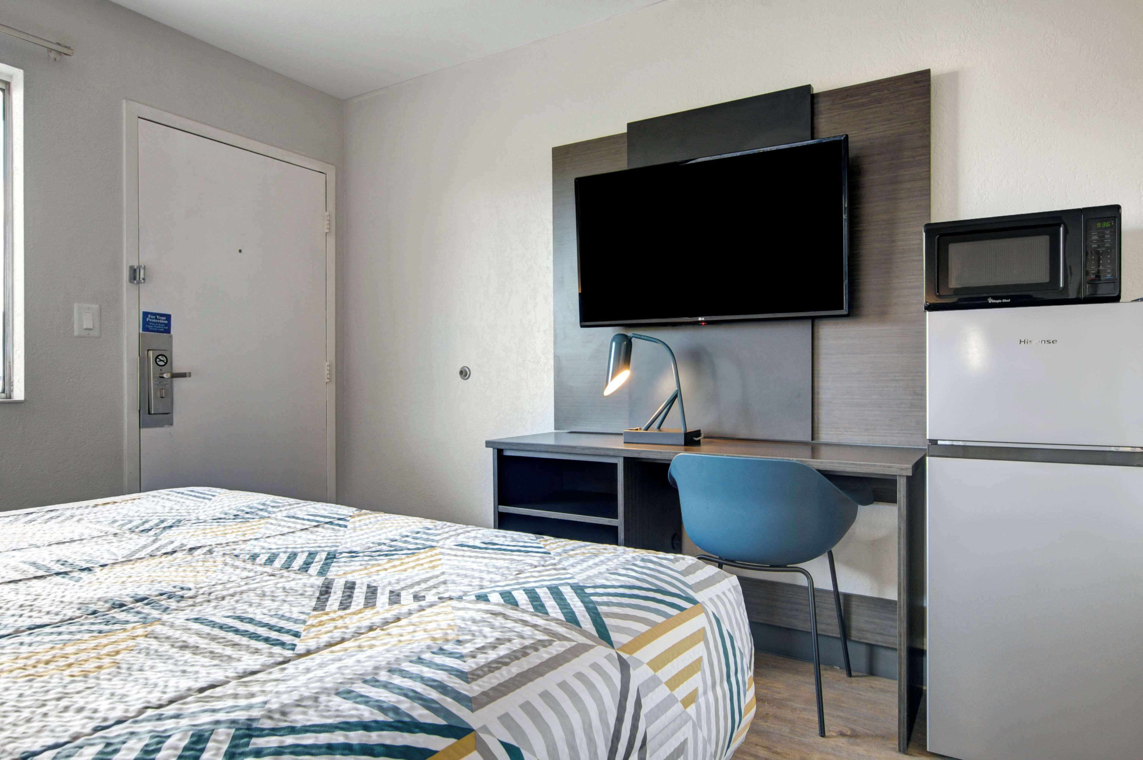 Une chambre d’hôtel équipée d’un lit, d’un bureau avec une chaise, d’un téléviseur à écran plat, d’un four à micro-ondes et d’un réfrigérateur.