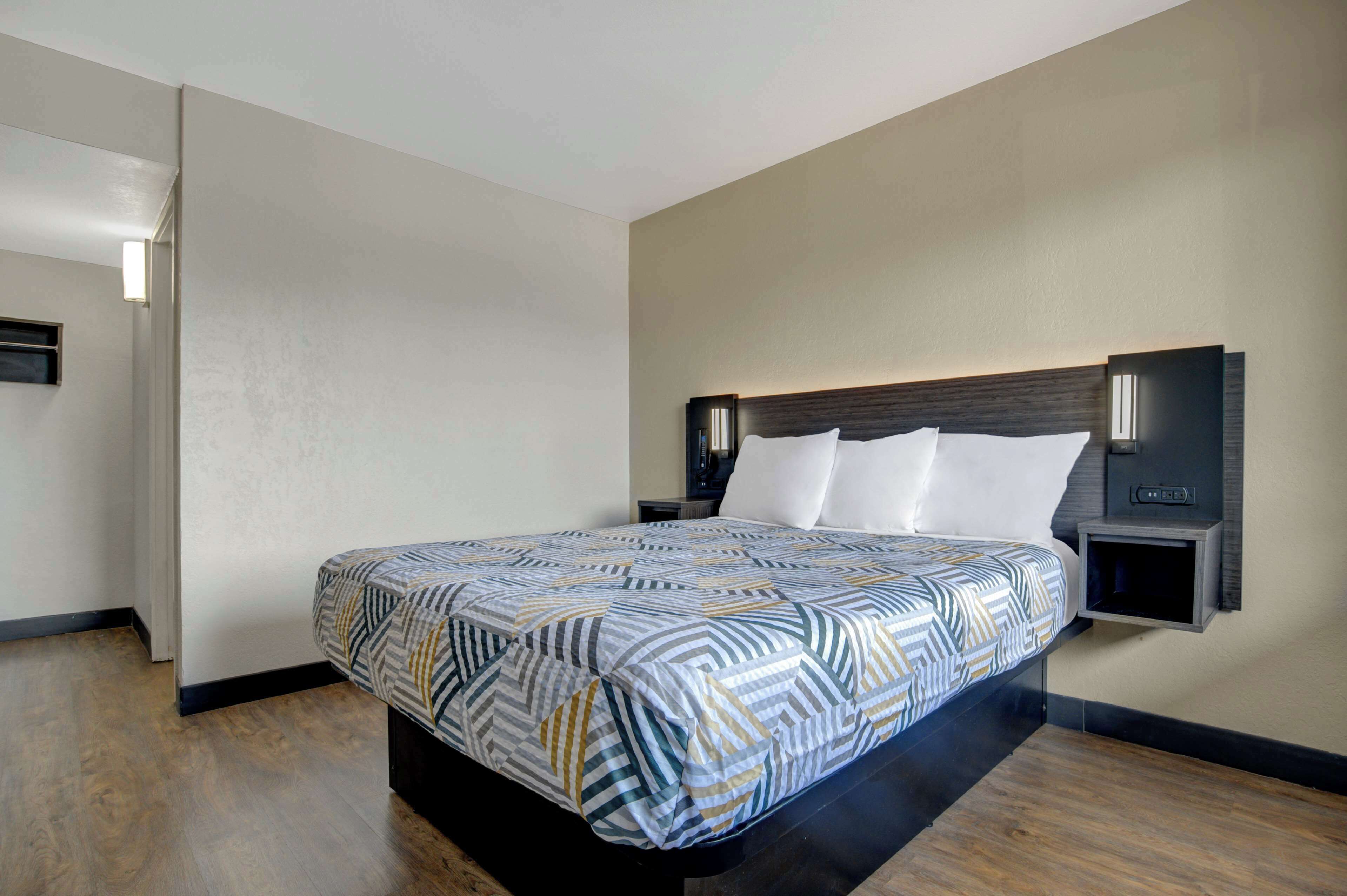 A modern hotel room with a large bed, a nightstand, and a wall-mounted reading light.